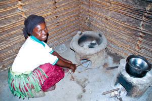 Stolze Besitzerin einer energie-effizienten Hersstelle. Diese wurde bei einer Fortbildung im Dorf Kighengi in Uganda erstellt. Sie spart Holz, die Zeit der Beschaffung und reduziert die Rauchbelastung.